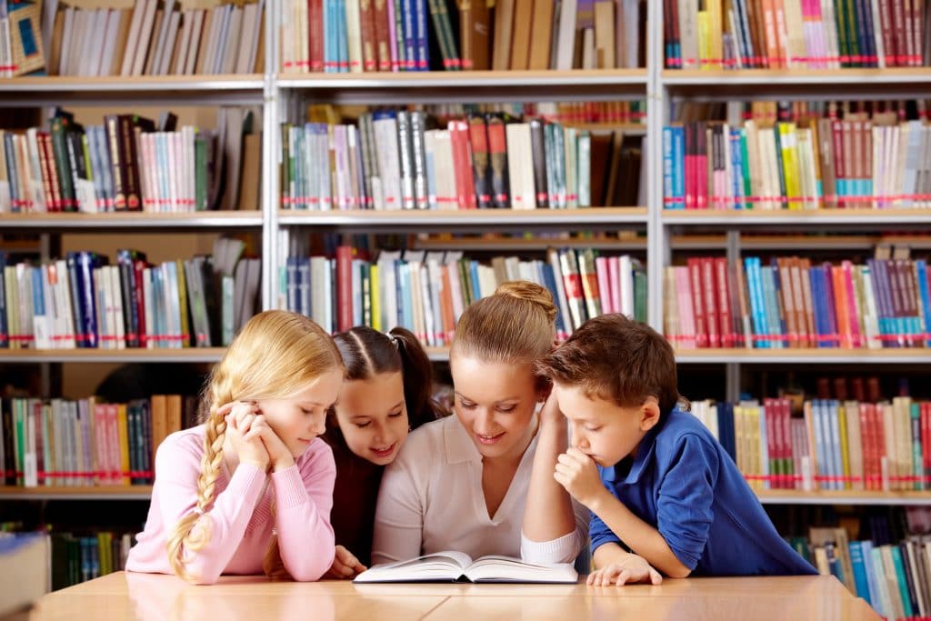 Teacher and children in a primary school library reading from resources found via a library system